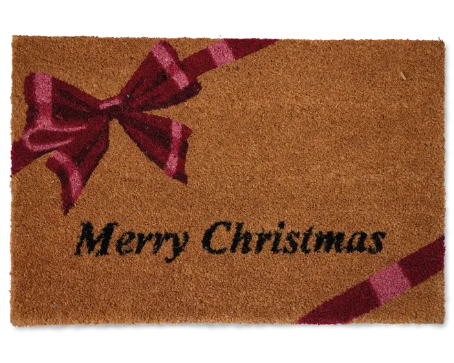 Rektangulært dørmåtte lavet af naturlige kokosfibre med et festligt design. Måtten har en stor rød sløjfe og bånd trykt diagonalt fra øverste venstre til nederste højre hjørne. Ordene "Merry Christmas" står skrevet med fed sort skrift i nederste venstre område. Baggrunden er varm, naturlig brun, og overfladen har en tekstureret, børstet struktur, der effektivt fjerner snavs fra sko.
