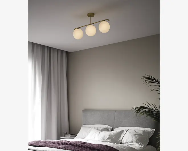 Loftlampe med tre jævnt fordelte, runde matterede glasglober monteret på en vandret metalstang i messingfarve. Lampen har et minimalistisk, moderne design og er monteret tæt på loftet, hvilket giver et blødt, diffust lys.