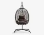 Hængende æggeformet stol med en flettet ramme i rattan-stil, understøttet af et robust metalstativ. Stolen har bløde, mørkebrune hynder til sidde- og rygstøtte samt en ekstra pude for øget komfort. Den åbne gitterstruktur giver god luftcirkulation og et moderne udseende.
