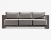 Moderne tresæders med tykke, lysegrå hynder på både sæde og ryg. Stellet er kantet og robust, lavet af et mat materiale i taupe eller lysebrun farve. Armlænene er brede og flade, hvilket giver ekstra overfladeplads. Designet er minimalistisk og nutidigt, velegnet til både indendørs og udendørs brug.