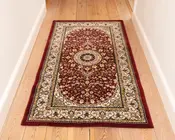 Rektangulært tæppe med en dyb rød baggrund og detaljerede blomster-mønstre i creme, guld og mørkeblå. Tæppet har et centralt medaljon-design omgivet af symmetriske motiver, og en bred cremefarvet kant dekoreret med snoede vinranker og blomsterdetaljer. Kanterne er afsluttet med en ensfarvet rød kant. Tæppet ser blødt ud og passer godt til en gang eller et smalt rum.