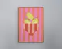 Indrammet kunstværk med en stiliseret illustration af tre gule frugter med grønne stilke i en rød- og lyserødstribet skål. Baggrunden består af lodrette, skiftevis lyserøde og røde striber, hvilket giver et markant og moderne udtryk. Rammen er enkel og lavet af lyst træ.