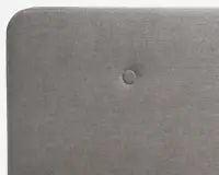 Nærbillede af en rektangulær, polstret overflade i lysegråt stof med en enkelt centralt placeret knap. Kanterne er blødt afrundede, og stoffet har en diskret vævet struktur.