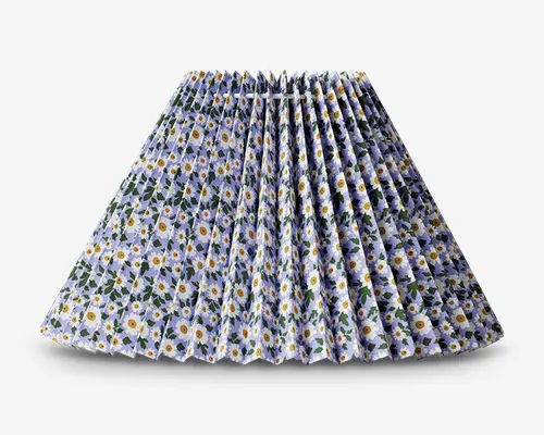 En plisseret nederdel med et livligt margueritmønster, hvor blomsterne har hvide kronblade og gule midter, på en lyseblå baggrund. Nederdelen har en struktureret, vid silhuet med skarpe, jævnt fordelte læg, der giver volumen og bevægelse. Linningen ser tætsiddende ud, og det samlede design giver et friskt, sommerligt udtryk.