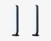 Et par slanke, lodrette LED-lysstænger med afrundede kanter, monteret på cirkulære sorte baser. Lysene har et moderne, minimalistisk design med en hvid oplyst front og en mat sort bagside. Velegnet til placering på skrivebord eller hylde og giver stemnings- eller accentbelysning.