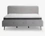 En moderne sengeramme med et lysegråt polstret hovedgærde og fodgærde, begge med knapdetaljer. Sengen står på fire skrå træben, hvilket giver et moderne udtryk. Madrassen er hvid med quiltet mønster og har en mørkegrå kant, hvilket giver et rent og stilfuldt udseende.