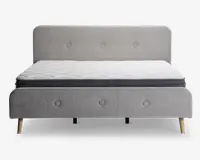 En moderne sengeramme med et lysegråt polstret hovedgærde og fodgærde, begge med knapdetaljer. Sengen står på fire skrå træben, hvilket giver et moderne udtryk. Madrassen er hvid med quiltet mønster og har en mørkegrå kant, hvilket giver et rent og stilfuldt udseende.