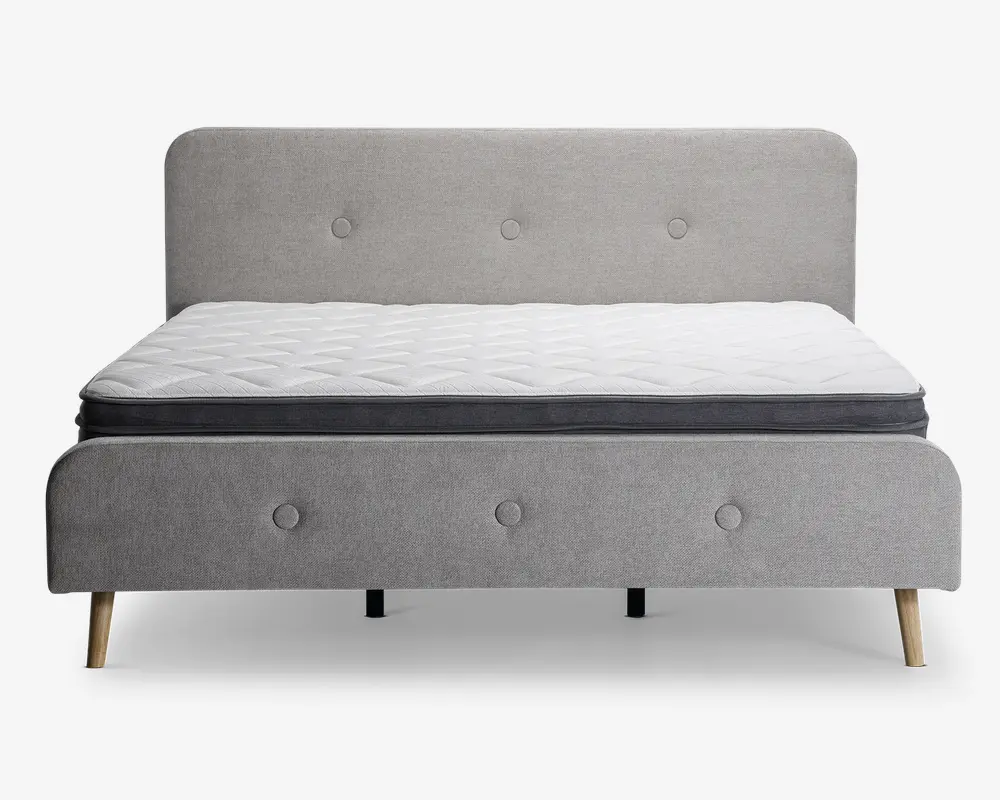 En moderne sengeramme med et lysegråt polstret hovedgærde og fodgærde, begge med knapdetaljer. Sengen står på fire skrå træben, hvilket giver et moderne udtryk. Madrassen er hvid med quiltet mønster og har en mørkegrå kant, hvilket giver et rent og stilfuldt udseende.