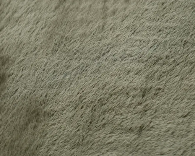 Nærbillede af et blødt materiale med kort luv og en diskret, naturlig tekstur. Overfladen fremstår glat med fine, tætte fibre i en afdæmpet grågrøn farve, hvilket giver et plysset og hyggeligt udtryk. Teksturen er ensartet med lette variationer i nuancer og fibrenes retning.