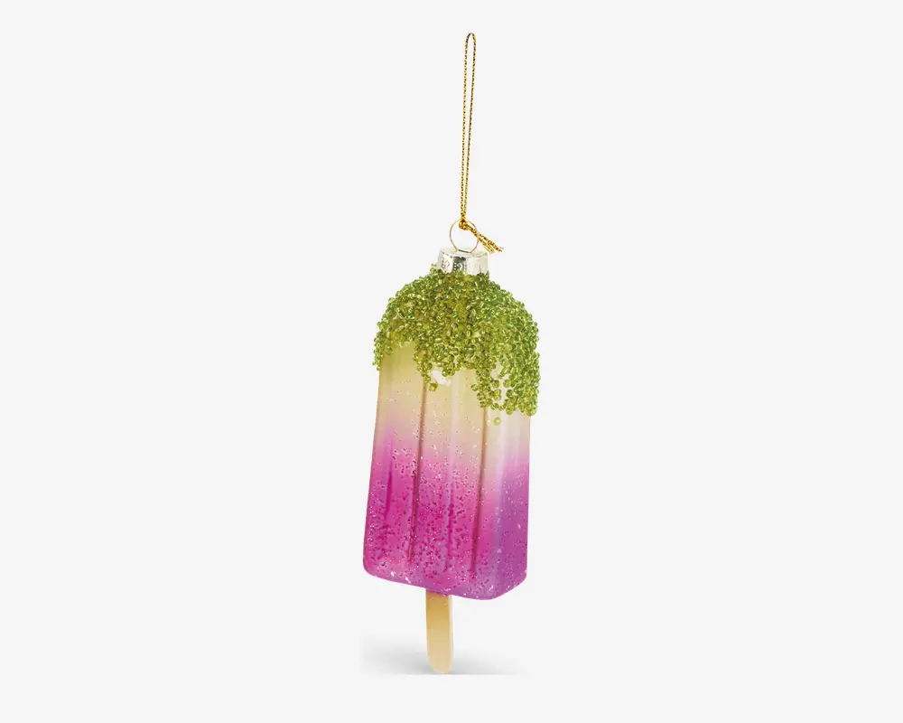 En dekorativ ornament formet som en ispind, med et farveforløb fra lysegul i toppen til kraftig pink i bunden. Toppen er dækket af grøn glimmer, der ligner drys eller hakkede nødder, og ornamentet hænger i en gylden snor. Overfladen er blank og glitrende, og en lille træpind stikker ud i bunden, som på en rigtig ispind.