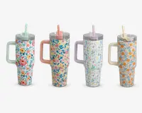 Fire høje, cylindriske drikkebeholdere med store sidehåndtag og gennemsigtige låg med indbyggede sugerør. Hver beholder har et unikt blomsterdesign i pastelfarver: Den første har hvid baggrund med lyserøde, orange og blå blomster samt mintgrønt håndtag og sugerør; den anden har ferskenfarvet baggrund med blå og lyserøde blomster, ferskenfarvet håndtag og lyserødt sugerør; den tredje har hvid baggrund med små flerfarvede blomster, lavendelfarvet håndtag og lyse lilla sugerør; den fjerde har hvid baggrund med orange og blå blomster, cremefarvet håndtag og sugerør.