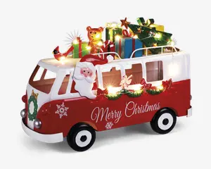 En festlig rød og hvid varevogn dekoreret med juletema. Varevognen har teksten 'Merry Christmas' på siden, snefnugmotiver og en grøn krans foran. En tredimensionel julemandsfigur sidder i førervinduet. På taget er der stablet farverige indpakkede gaver, en bamse, et juletræ og en gul stjerne. Hele dekorationen er oplyst af små, varme hvide LED-lys, som giver et hyggeligt og festligt udtryk.
