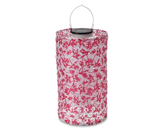 Cylindrisk lanterne med lyserødt blomstermønster på hvid baggrund, udstyret med et metalhåndtag øverst for nem transport. Lanternens gennemsigtige krop lader lyset skinne igennem og skaber en dekorativ effekt. Toppen er solid med en sort detalje omkring håndtagets fastgørelse.
