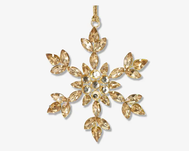 Et dekorativt ornament formet som en snefnug, med flere guldfarvede, facetslebne krystaller arrangeret i et symmetrisk mønster. Krystallerne er marquise-slebne og runde, hvilket giver en glitrende effekt. Ornamentet har en guldfarvet løkke øverst til ophængning.