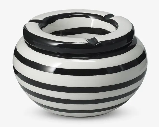 Rund keramisk beholder med bred åbning og skiftevis sorte og hvide vandrette striber. Randen er tyk og har en udskæring, sandsynligvis til at hvile en cigaret. Den blanke overflade giver et stilrent og moderne udtryk.