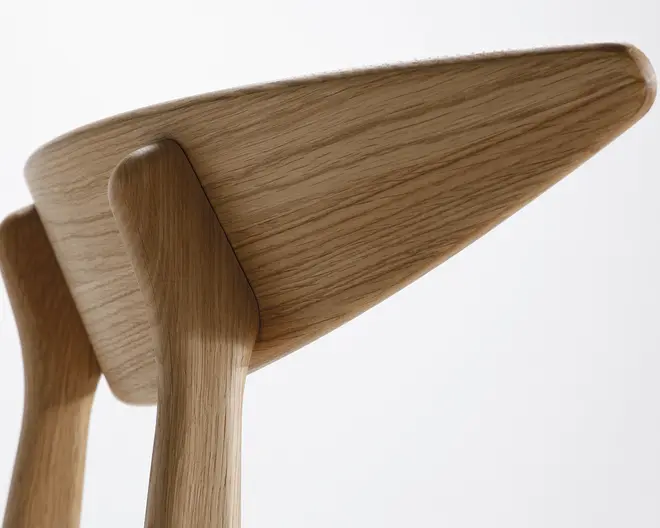 Nærbillede af et møbel i træ med glatte, afrundede kanter og en naturlig, lys egetræsfinish. Håndværket fremhæver sømløse samlinger og et minimalistisk, moderne design med synlige åretegninger i træet.