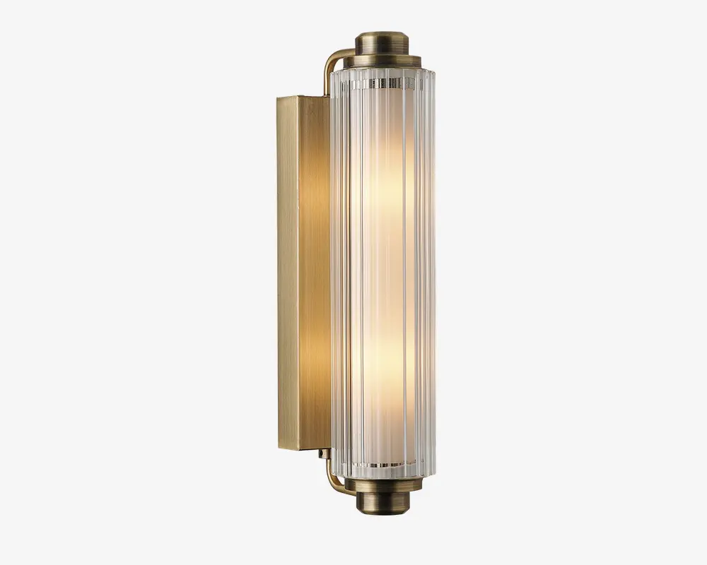 Væghængt lampe med cylindrisk glasskærm med lodrette riller, fastgjort i en ramme af børstet messing. Lampen udsender et varmt, diffust lys og har et moderne, elegant design med metalliske detaljer og klart glas.