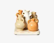 Et sæt med seks små keramikkander i forskellige former og størrelser, arrangeret på et rektangulært, plettet keramisk fad. Kanderne har runde kroppe med to eller tre hanke hver og kommer i varme jordfarver som creme, beige og lysebrun med en blank glasur. Det samlede design har et rustikt, håndlavet udtryk.