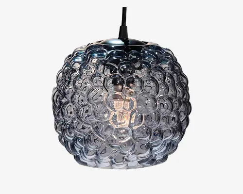 Kugleformet pendellampe med en tekstureret glasskærm, der har et boblelignende mønster. Glasset er klart med et let røgfarvet skær, hvilket giver et moderne og kunstnerisk udtryk. Overfladen har hævede cirkulære mønstre, som giver lampen et unikt og iøjnefaldende look. Pæren indeni er synlig og bidrager til det dekorative udtryk, når lampen er tændt.