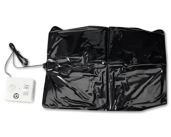 Billedet viser en rektangulær, blank sort måtte med en let krøllet overflade. Til måtten er der tilsluttet en hvid elektronisk kontrolenhed med ledning. Kontrolenheden har et gitter til højttaler, en drejeknap og trykte mærkater, hvilket indikerer justerbare indstillinger. Måtten virker fleksibel og er sandsynligvis beregnet til at blive placeret på en flad overflade. Det samlede design antyder, at den bruges sammen med elektroniske funktioner, muligvis til opvarmning, overvågning eller alarmering.