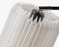 Nærbillede af en lampeskærm med geometrisk, plisseret design lavet af gennemsigtigt hvidt materiale. Skærmen har skarpe, kantede folder, der giver et tekstureret og moderne udtryk. Toppen af skærmen er fastgjort til en sort cylindrisk fatning med en metalarm, hvilket giver et nutidigt look.