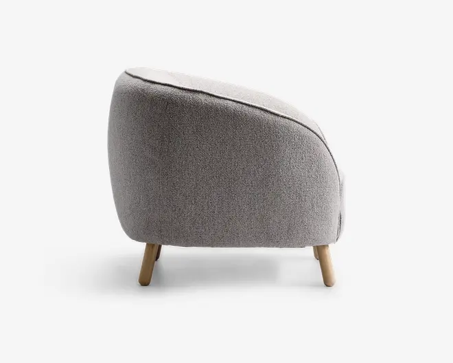 Sidevisning af en moderne stol med rundet, buet ryg og sæde betrukket med lysegråt, tekstureret stof. Stolen har korte, skråtstillede træben, hvilket giver den et moderne og hyggeligt udtryk.