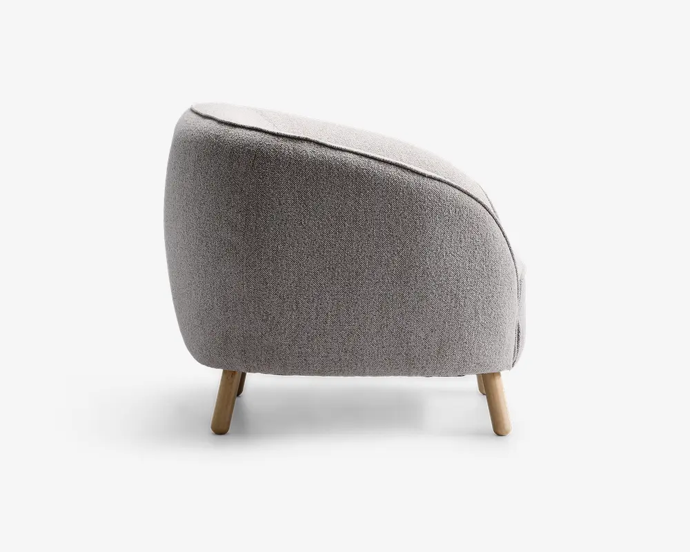 Sidevisning af en moderne stol med rundet, buet ryg og sæde betrukket med lysegråt, tekstureret stof. Stolen har korte, skråtstillede træben, hvilket giver den et moderne og hyggeligt udtryk.
