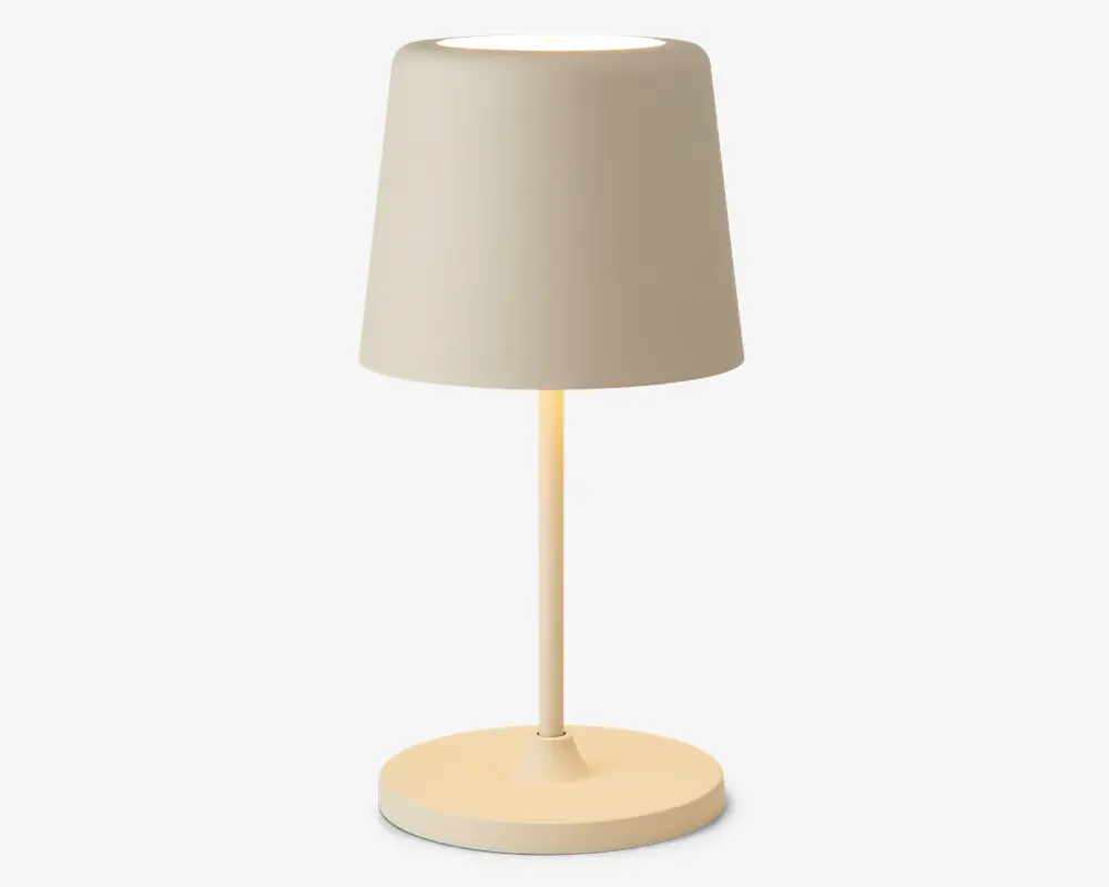 En moderne bordlampe med mat beige finish. Lampen har en cylindrisk fod, en slank, lige stang og en let konisk, tromleformet lampeskærm. Designet er minimalistisk, og lampen udsender et blødt, varmt lys fra toppen af skærmen.