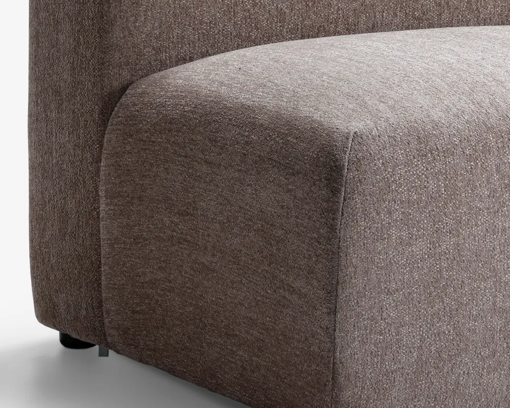 Nærbillede af et sofahjørne med en glat, afrundet armlæn og sæde. Betrækket er et tekstureret, mellembrunt stof med et diskret vævemønster. Designet er moderne og minimalistisk med rene linjer og et blødt, polstret udseende.