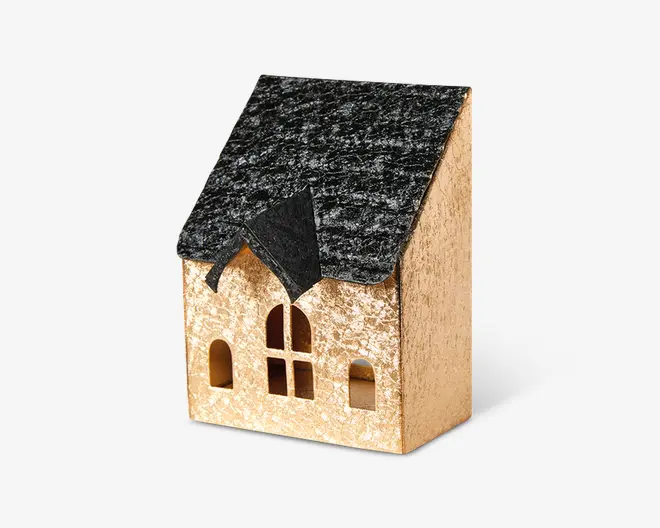 Lille dekorativt hus med en sort, tekstureret tag og en beige facade med let glimmer. Forsiden har tre buede vinduer og et centralt rektangulært vindue med krydsdesign samt en lille gavl over indgangen. Udseendet er rustikt og charmerende, velegnet til jule- eller boligindretning.