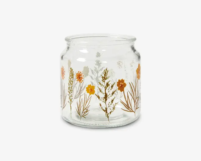 Klar glasbeholder med bred åbning og let rundet krop, dekoreret med et mønster af orange, gule og brune vilde blomster samt grønt løv. Blomstermotivet er trykt rundt om ydersiden og giver beholderen et botanisk og rustikt udseende.