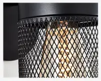 Nærbillede af en cylindrisk lampe med sort metalnet som skærm. Nettet har et diamantmønster, der lader det varme lys fra pæren indenfor skinne igennem. Lampen har en mat sort finish og et industrielt design.