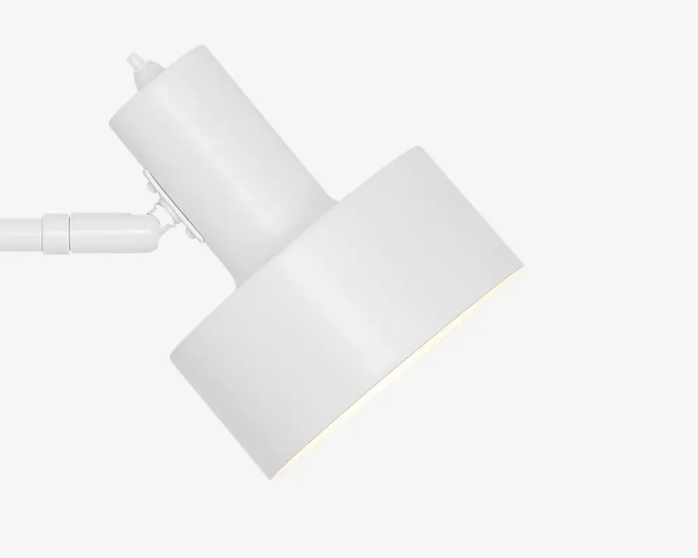En moderne, minimalistisk hvid spotlampe med cylindrisk lampehus og et rektangulært, let vinklet skærm. Lampen har en glat, mat overflade og et drejeled, så lysets retning kan justeres. Designet er stilrent og diskret, velegnet til moderne indretning.