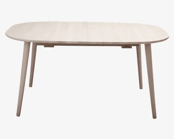 Lyst træbord med oval bordplade og fire skråtstillede ben. Bordpladen har en glat, naturlig finish og en diskret samling i midten, hvilket indikerer, at den muligvis kan udvides. Benene er let tilspidsede og placeret i hjørnerne for stabilitet.