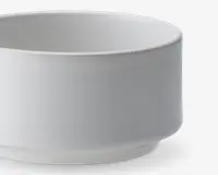 En enkel, hvid, cylindrisk skål med glatte sider og en let hævet bund. Skålen har et minimalistisk design uden mønstre eller dekorationer og en mat overflade.