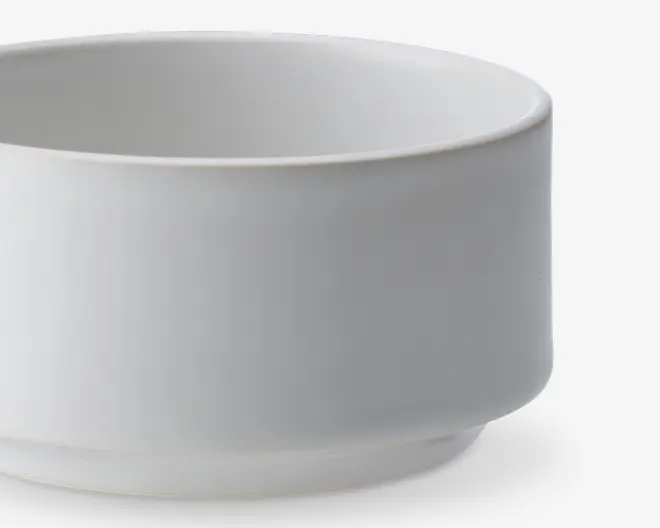 En enkel, hvid, cylindrisk skål med glatte sider og en let hævet bund. Skålen har et minimalistisk design uden mønstre eller dekorationer og en mat overflade.