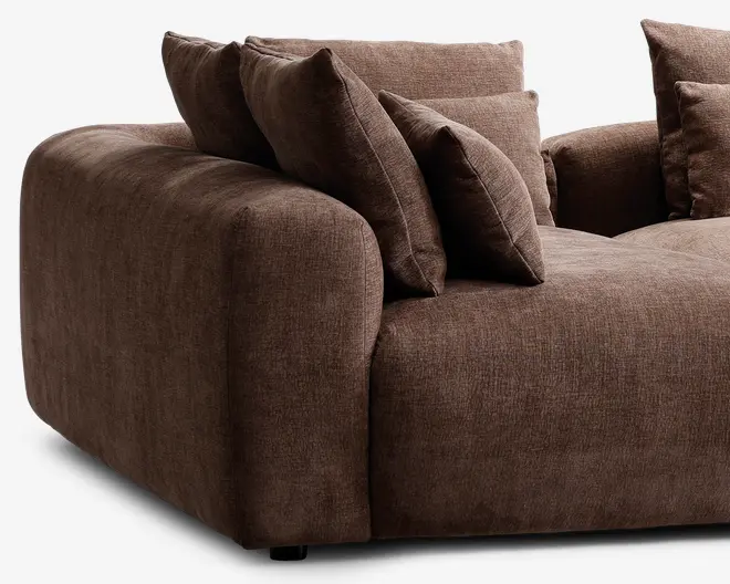 Blød, moderne siddeplads med brede, afrundede armlæn og dybt sæde. Polstret med et blødt, tekstureret brunt stof og udstyret med flere store, matchende ryg- og sidepuder for ekstra komfort og støtte. Det samlede design er indbydende og moderne, ideelt til afslapning.