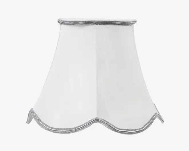 Hvid lampeskærm med udsvunget, bølget bundkant og diskret sølvkant langs top og bund. Stoffet virker glat og let gennemsigtigt, hvilket giver et blødt og elegant udtryk. Formen er let buet og tilføjer et dekorativt præg.