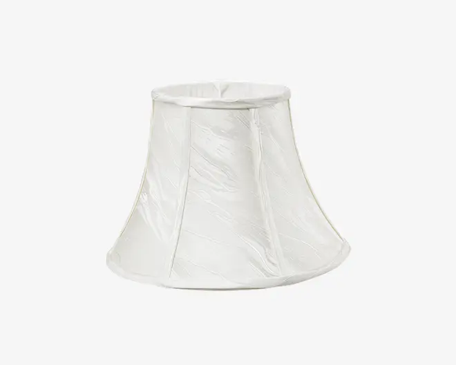 En klokkeformet lampeskærm lavet af hvidt stof med en let krøllet struktur. Skærmen har lodrette stofpaneler adskilt af smalle syninger, og både øverste og nederste kant er afsluttet med en glat stofkant. Udtrykket er klassisk og elegant, velegnet til traditionel eller tidløs indretning.