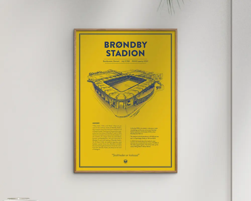 En indrammet plakat med en klar gul baggrund og en tynd sort kant. Plakaten viser en detaljeret, håndtegnet illustration af et stadion i blå blæk, placeret over midten. Titlen 'BRØNDBY STADION' står med store, fede blå bogstaver øverst. Under illustrationen er der et tekstafsnit, der giver historisk information om stadionet, også i blå. Designet er minimalistisk og moderne med en stærk kontrast mellem den gule baggrund og det blå motiv og tekst.