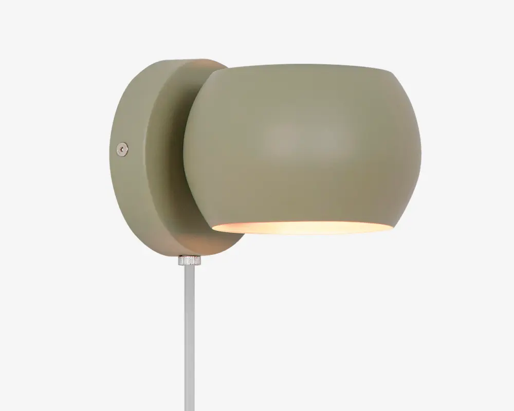 En moderne vægmonteret lampe med mat olivengrøn finish. Lampen har en rundet, let oval lampeskærm, der leder lyset nedad. Armaturet er fastgjort til en cirkulær vægplade, og en hvid ledning går ud fra bunden. Designet er minimalistisk og nutidigt, velegnet til forskellige indretninger.