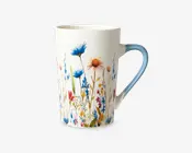 Høj keramikkop med hvid baggrund og et farverigt design af vilde blomster. Blomsterne er i blå, rød, gul og orange nuancer med grønne stilke og blade, hvilket giver et livligt og naturligt udtryk. Hanken er let buet og har en blød overgang til lyseblå, som matcher blomsterdekorationen.