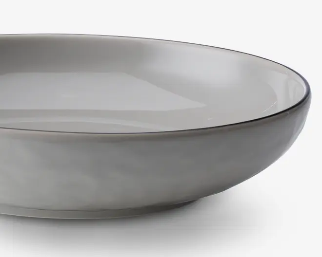 En rund, lav skål med en glat, mat lysegrå yderside og en blank lysegrå inderside. Skålen har en let hævet kant med en diskret, mørkere grå kant. Designet er minimalistisk og moderne med rene linjer og en blødt buet profil.