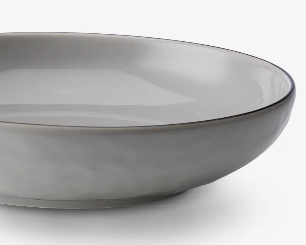 En rund, lav skål med en glat, mat lysegrå yderside og en blank lysegrå inderside. Skålen har en let hævet kant med en diskret, mørkere grå kant. Designet er minimalistisk og moderne med rene linjer og en blødt buet profil.