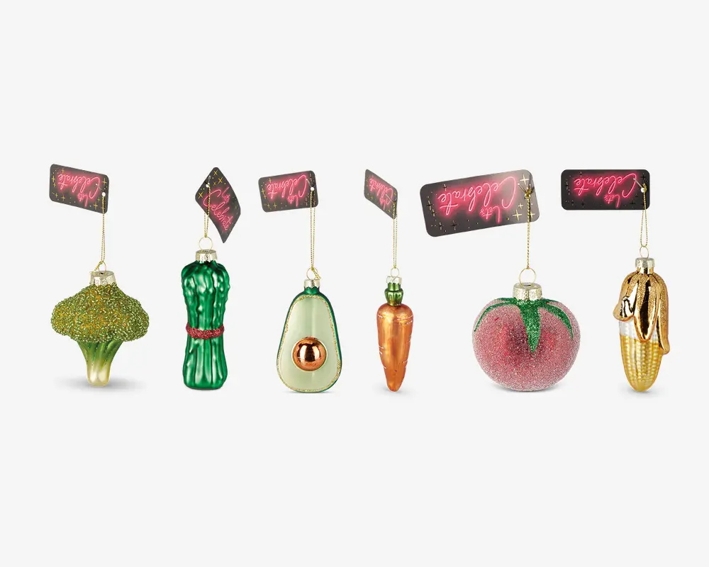 Sæt med seks glasornamenter formet som forskellige frugter og grøntsager, herunder broccoli, asparges, avocado, gulerod, fersken og majs. Hvert ornament er detaljeret med levende farver og glimmerdetaljer og har en gylden ophængssnor med et lyserødt mærke.