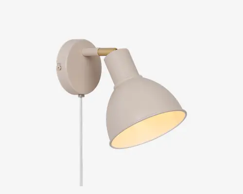 Væghængt lampe med mat beige finish og konisk lampeskærm. Lampen har en rund base, en kort arm med messingdetalje og en synlig hvid ledning, der hænger ned. Indersiden af skærmen er hvid, hvilket giver et varmt og fokuseret lys. Lampens hoved kan justeres, så lyset kan rettes i forskellige retninger.