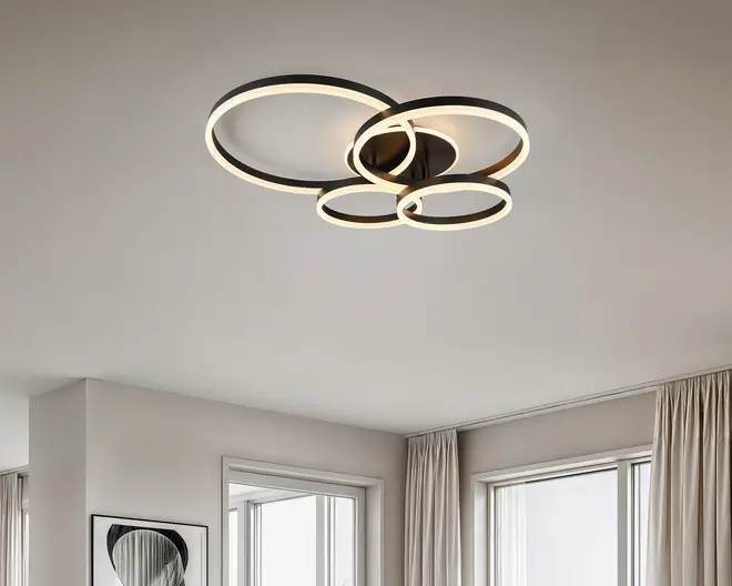 Loftmonteret lampe med et moderne design bestående af fire sammenhængende LED-ringe i forskellige størrelser. Ringene har en mat sort finish og integreret, diffust lys, der giver en blød og jævn belysning. Lampen sidder tæt på loftet og egner sig derfor til rum med lavere lofthøjde. Det geometriske og minimalistiske udtryk passer godt til moderne indretning.