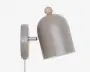 Væglampe med mat taupefarvet afrundet skærm, en lille træknop på toppen og en cylindrisk metalbase med en kort justerbar arm.