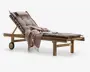 Justerbar liggestol i træ med tykke, polstrede brune hynder for ekstra komfort. Stolen har en tilbagelænet ryg, to hjul for nem flytning og en solid ramme. Et tekstureret, frynset tæppe i støvet rosa farve er lagt over sædet, og et par solbriller ligger på hynden, hvilket giver et indtryk af afslapning udendørs.