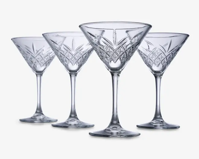 Sæt med fire klare glas med stilk, hver med en bred, konisk skål og indviklede geometriske mønstre skåret i den nederste del af skålen. Glassene har en solid fod og elegante, lange stilke, hvilket giver dem et sofistikeret og klassisk udseende.
